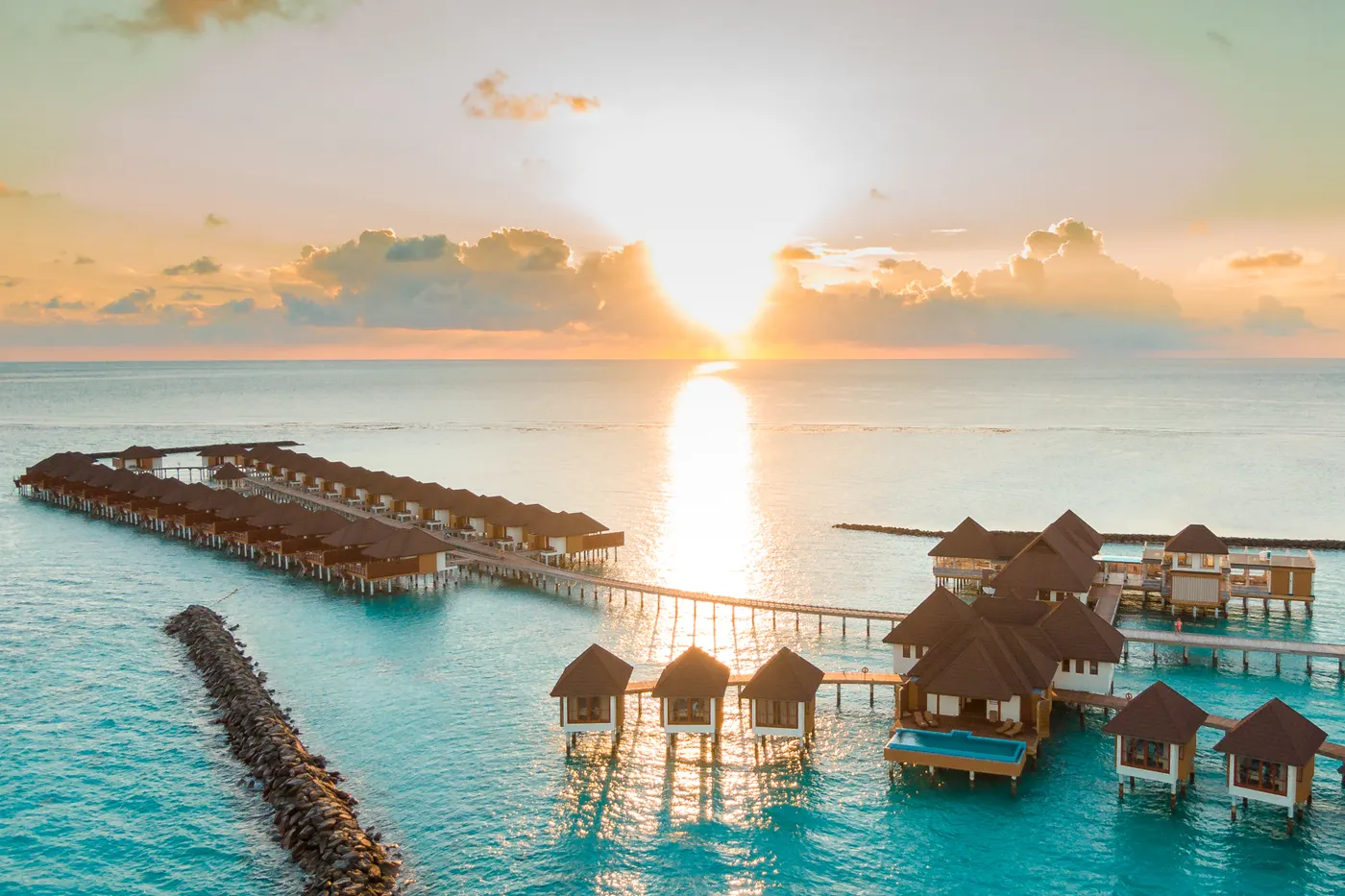Golden-hour aerial view of overwater bungalows at a premium tropical resort